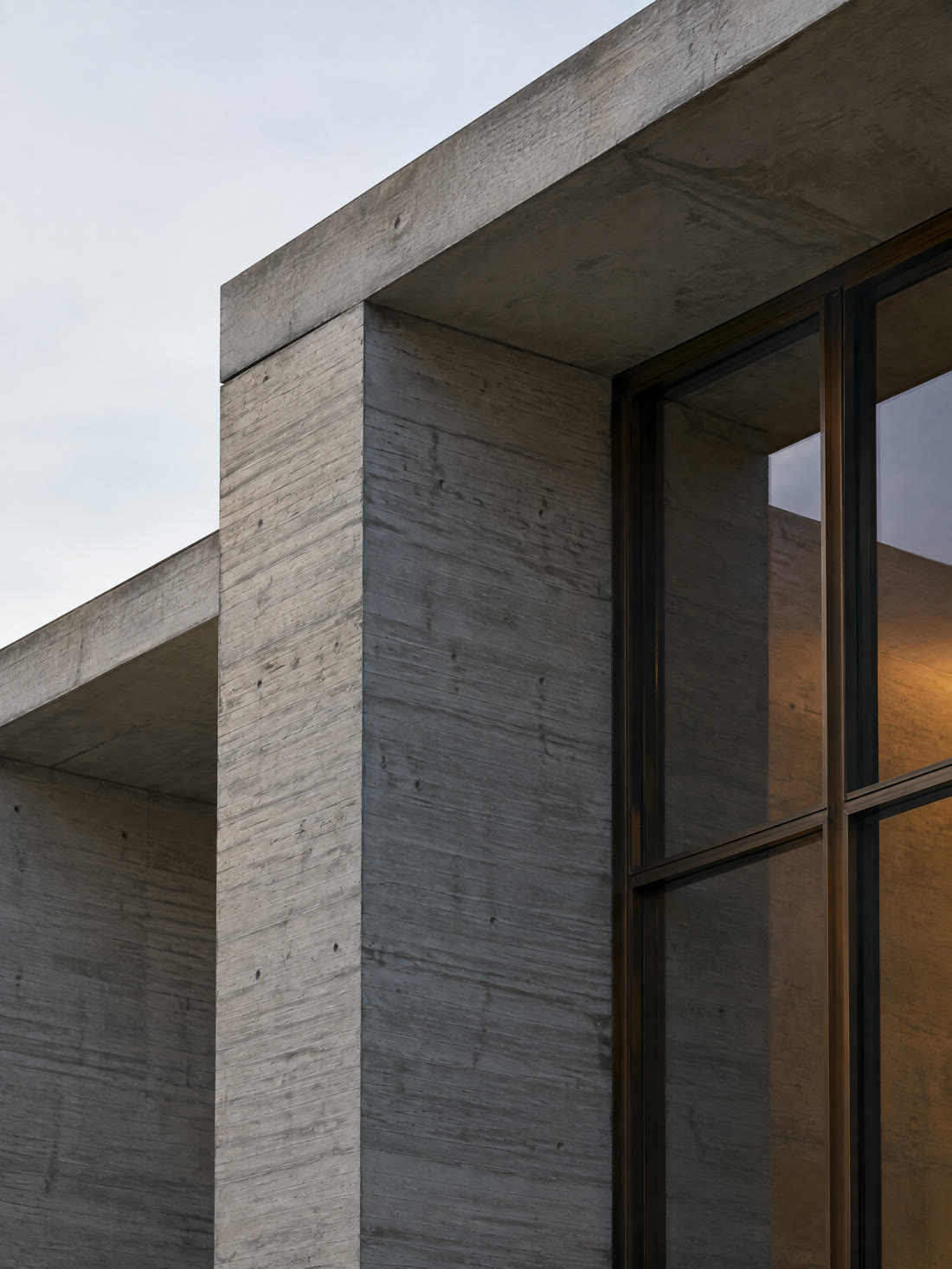 Concept image: close detail where a board-formed concrete column meets a slab edge and a bronze window frame.